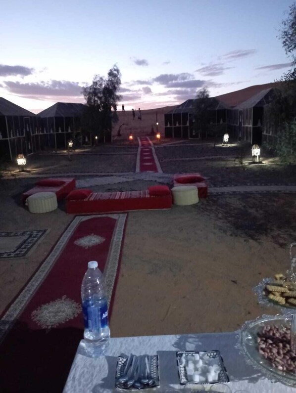 A dining area with a table set for a meal, a bottle of water, and snacks. - Merzouga Yawza Camp (Taouz)