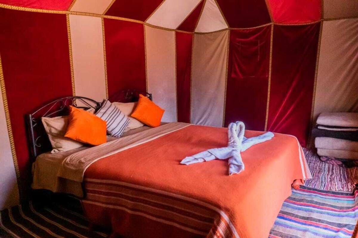 Una cama con una colcha a rayas, una almohada blanca y roja a rayas, y una almohada naranja.
