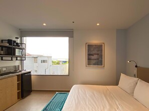 A modern hotel room with a bed, a kitchenette, a window with a view of buildings, and a framed artwork on the wall. - w* | Tranquil Loft w/ Great Terrace in Bocagrande (Cartagena de Indias)