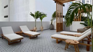 A rooftop lounge area with wooden loungers, potted plants, and a patterned floor. - w* | Tranquil Loft w/ Great Terrace in Bocagrande (Cartagena de Indias)