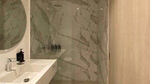 A bathroom with a marble wall, a round mirror, a white sink, and a shower area. - w* | Tranquil Loft w/ Great Terrace in Bocagrande (Cartagena de Indias)