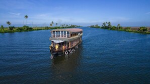 Una casa flotante con cubierta superior protegida y terraza inferior abierta, navegando en un río tranquilo.