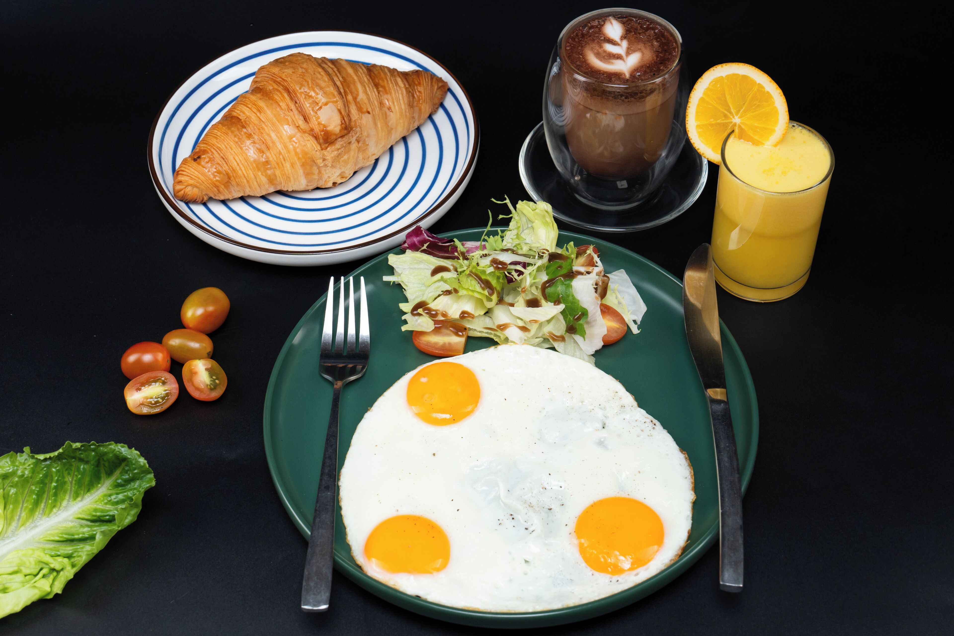 A breakfast plate with eggs, a croissant, a glass of orange juice, and a cup of coffee.