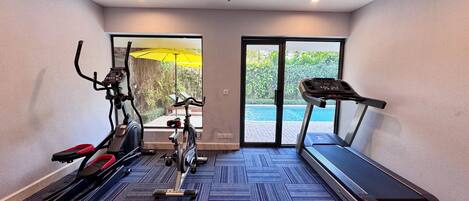 Un gimnasio con equipo de cardio, cinta de correr y vistas a una piscina.