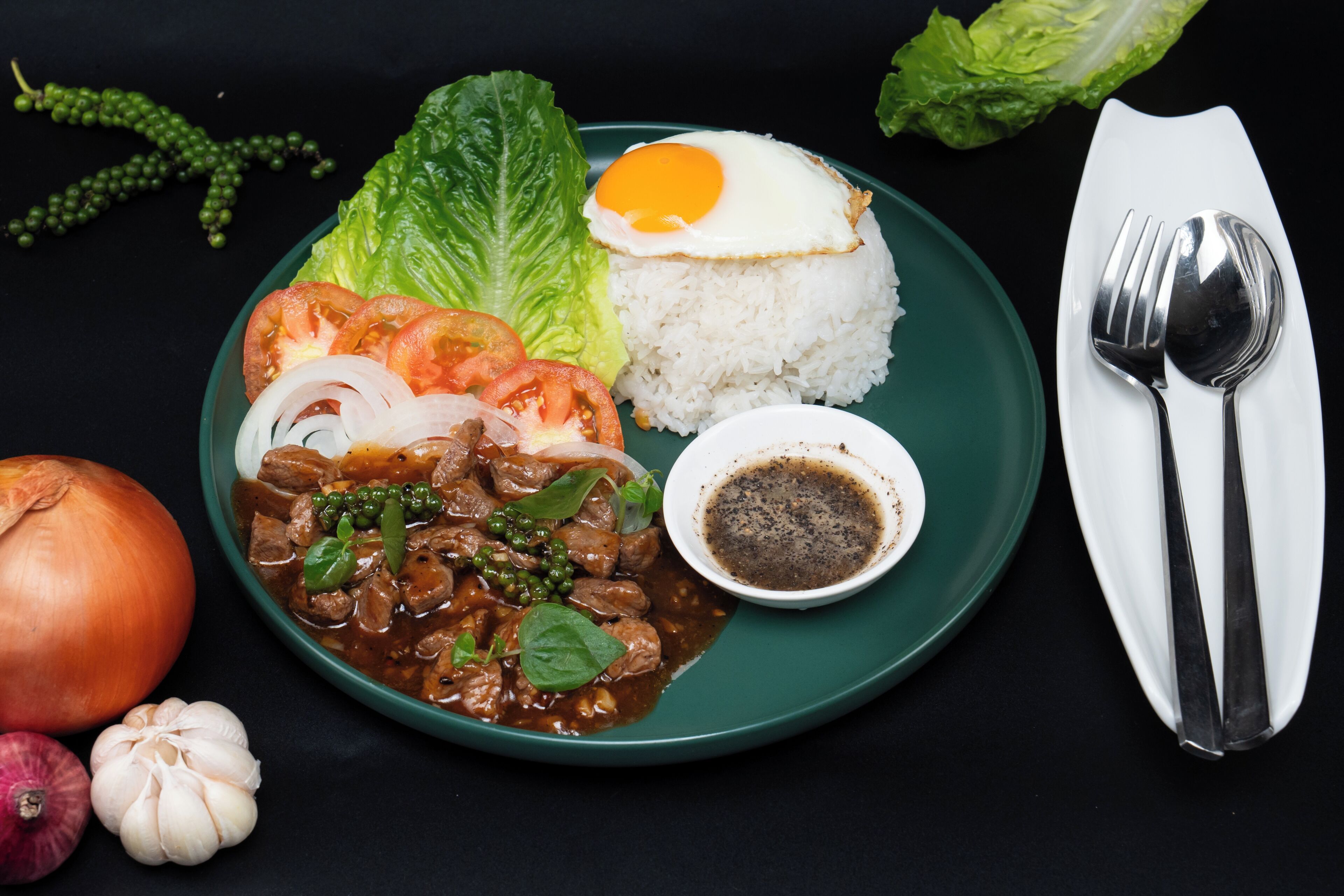 A plate with rice, a fried egg, vegetables, and a bowl of sauce.
