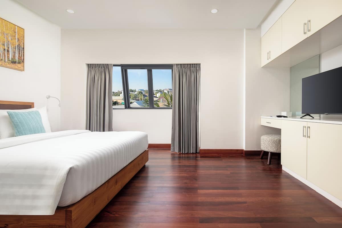 A bedroom with a bed, a desk, a TV, and a window with curtains.
