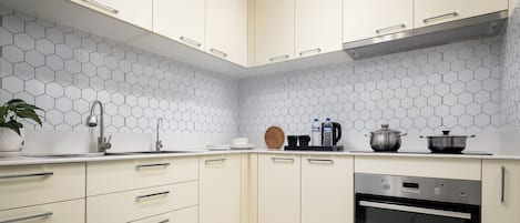 A modern kitchen with hexagonal tile backsplash, stainless steel appliances, and light-colored cabinetry.