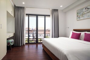 Hotellihuone, jossa on sänky, työpöytä, tuoli ja parveke, jolta on näkymä.
