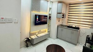 A modern kitchen with a built-in TV, grey cabinets, and a window with blinds. - 1Bed&Parlour(B3)@Lekki PH 1.24/7 Pwr By NgoZiLivin

 (Lekki)