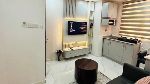 A modern living room with a flat-screen TV mounted on the wall, a grey cabinet, and a round coffee table. - 1Bed&Parlour(B3)@Lekki PH 1.24/7 Pwr By NgoZiLivin

 (Lekki)