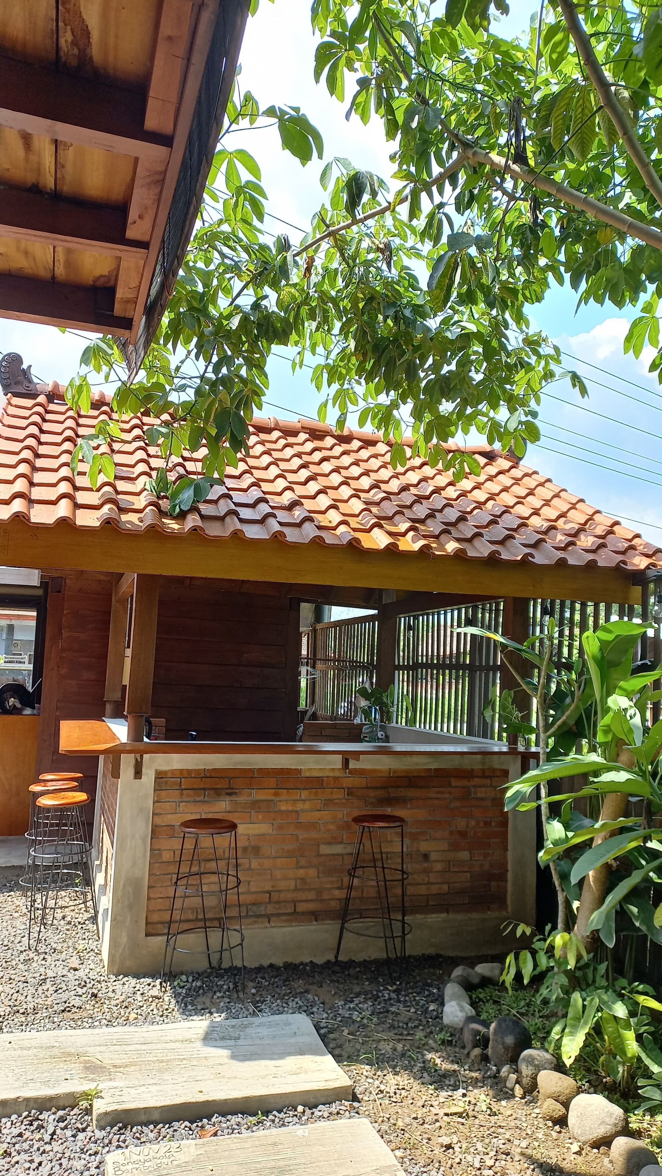 A rustic outdoor bar area with a tiled roof, wooden stools, and a brick counter.