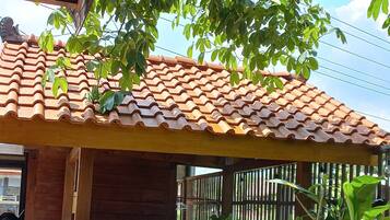 A rustic outdoor bar area with a tiled roof, wooden stools, and a brick counter.