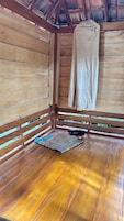 Una habitación de madera con un banco, una manta y ropa colgada.