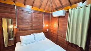 A wooden room with a bed, a mirror, and an air conditioning unit. - Sandyakala Borobudur (Borobudur)