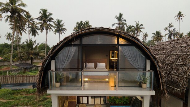 A thatched-roof bungalow with a balcony, a bed, a small pool, and a view of palm trees. - Tira Beach Resort (Varkala)