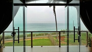 A modern room with a large glass door leading to a balcony with a view of the ocean. - Tira Beach Resort (Varkala)