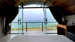 A spacious room with a large glass door leading to a balcony overlooking the sea. - Tira Beach Resort (Varkala)