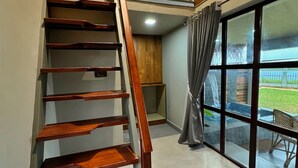 A wooden staircase leading to a second floor with a view of an outdoor patio through large windows. - Tira Beach Resort (Varkala)