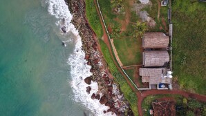 An aerial view of a coastal property with a beach, rocky shoreline, and thatched-roof structures. - Tira Beach Resort (Varkala)