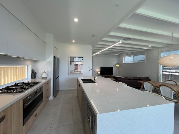 A modern kitchen with a central island, a dining area with a table and chairs, and a living room with a sofa and TV.