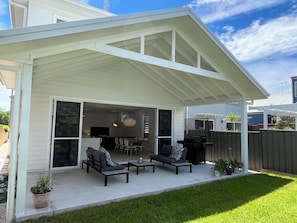 A covered patio with outdoor furniture, a grill, and a view of the backyard.