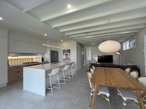 A modern kitchen with a central island, bar stools, and a dining area with a wooden table and chairs.
