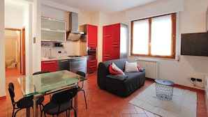 A compact kitchen with red cabinets, a glass dining table, and a black sofa. - Pratovecchio Suite (Florence)