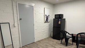 A small, modern kitchen with white brick walls, a grey door, a black refrigerator, a microwave, and a dining table with two chairs. - Rotorua Studio in a peaceful location. (Rotorua)