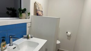 A bathroom with a white sink, blue tiles, a toilet, and a wooden floor. - Rotorua Studio in a peaceful location. (Rotorua)