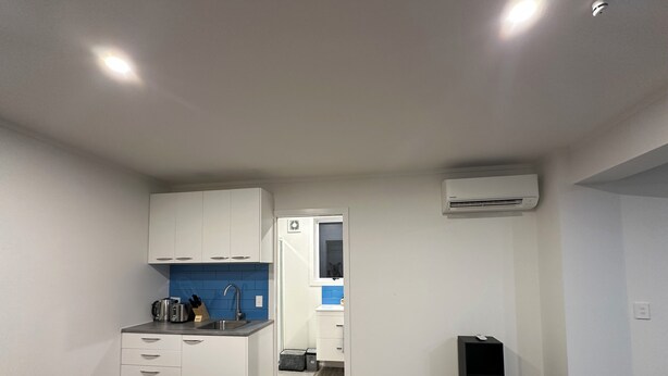 A compact kitchen with white cabinets, a blue backsplash, and a black speaker. - Rotorua Studio in a peaceful location. (Rotorua)