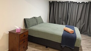 A bedroom with a bed, a wooden dresser, and a window with curtains. - Rotorua Studio in a peaceful location. (Rotorua)