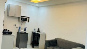 A compact room with a grey sofa, a small kitchenette with a microwave, a cabinet, and a desk with a chair. - 1Bed&Parlour(B2) @ Lekki PH 1.24/7 Pwr By NgoZiLivin

 (Lekki)