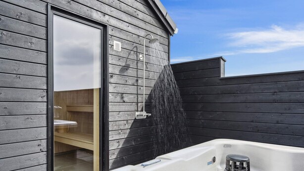 Een wellnessruimte met een jacuzzi, een houten blokhut en een houten terras.