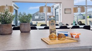 Een moderne keuken met een groot raam, potplanten, een juspak en twee broodjes op een snijplank.