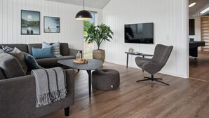Een moderne woonkamer met een grijze bank, een ronde salontafel, een grijze fauteuil en een aan de muur bevestigde televisie.