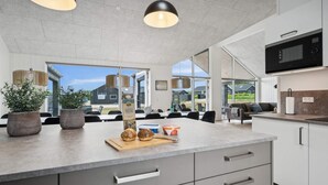 Een moderne keuken met grijze kastjes, een groot eiland met een snijplank, en een magnetron boven het aanrecht.