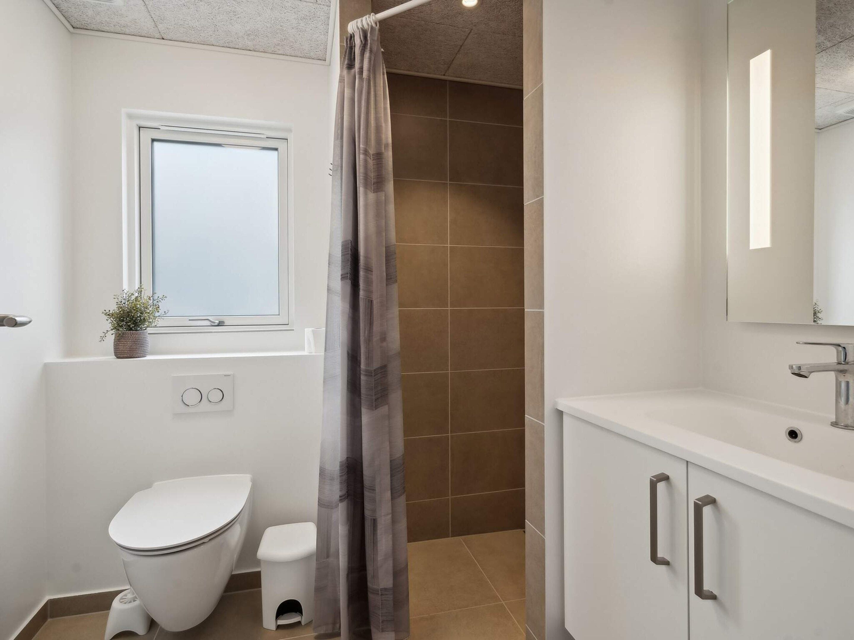 A bathroom with a toilet, a sink, a mirror, and a shower curtain.