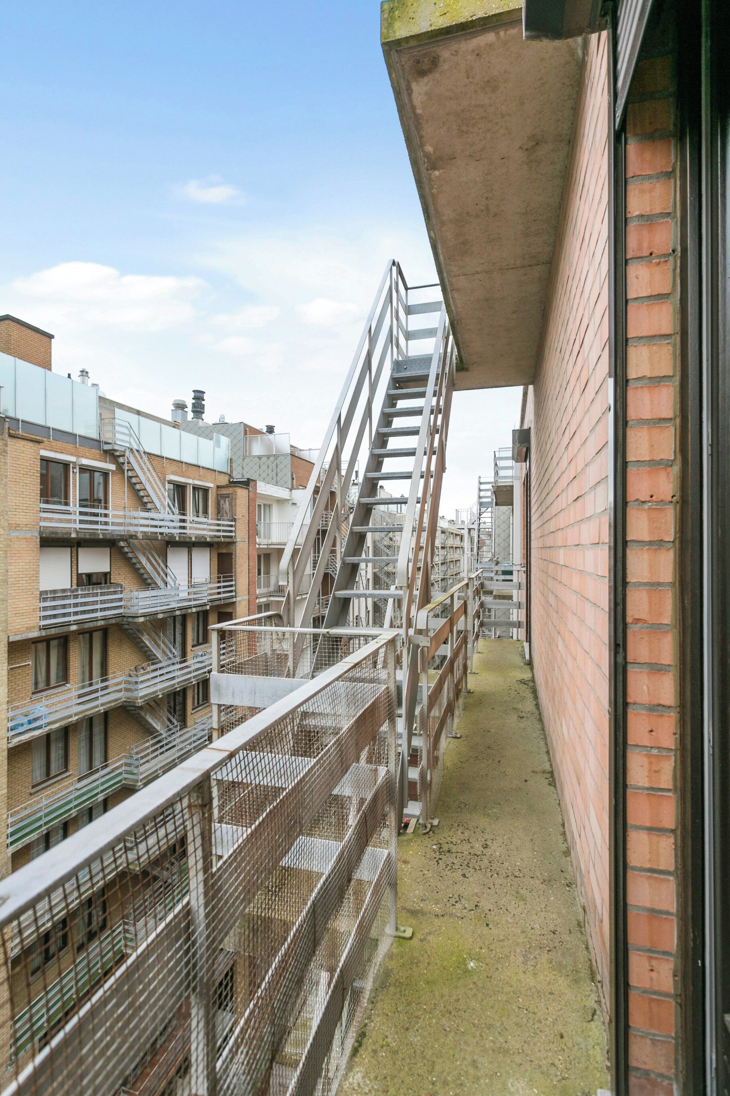 A narrow alleyway with a brick building on one side and a multi-story residential building with external staircases on the other.
