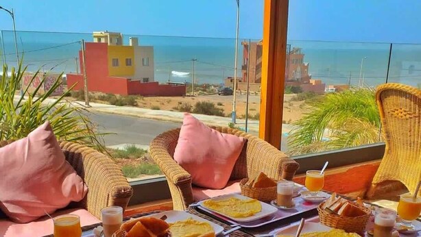 Colazione con mobili in vimini, vista sul mare e una cittadina costiera sullo sfondo.