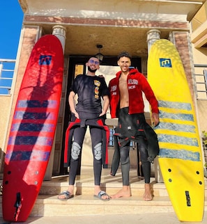 Two individuals standing in front of a building with surfboards. - golden twilight (Imsouane)