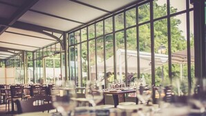 An indoor dining area with tables set for service, large windows, and a view of greenery outside. - IL MAESTRO - HOTEL RESTAURANT DU CHATEAU (Ecouen)