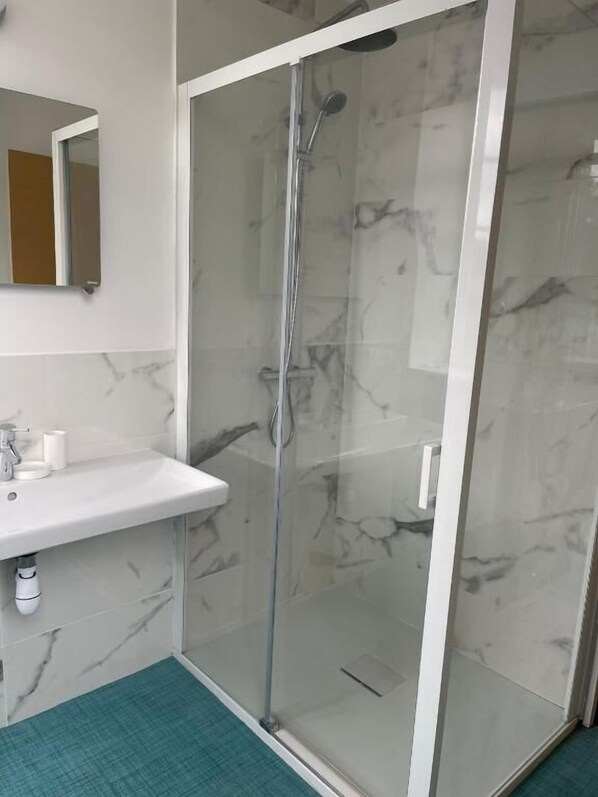 Un baño moderno con ducha de vidrio, un lavabo blanco y pared con azulejos de mármol.