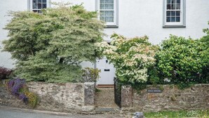 Un edificio blanco con tres ventanas, un muro de piedra con una reja, y un letrero que dice 'HALL HOUSE'.