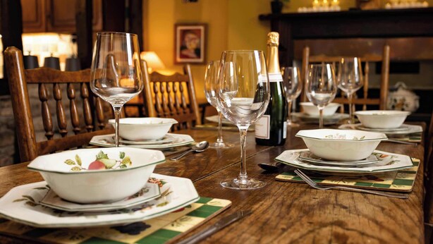 Una mesa de comedor dispuesta con varias copas de vino, cuencos y platos, con una botella de champán y velas sobre la mesa.
