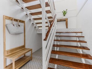 Una scala con gradini in legno e ringhiere bianche, un cesto intrecciato appeso al muro e una piccola pianta in vaso sul pianerottolo.