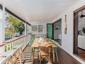 Un'area pranzo all'aperto coperta con tavolo e sedie in legno, un parapetto bianco e vista sulla strada.