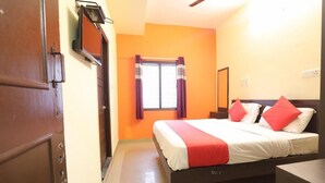 Habitación de hotel con cama, mesita de noche, ventana con cortinas, televisor montado en la pared y puerta.