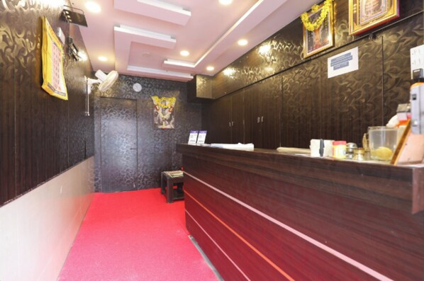 Un espace d’accueil avec un tapis rouge, un comptoir de réception en bois et un petit tabouret.