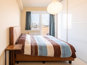 A bedroom with a large bed, a nightstand, a window with curtains, and a view of the outside. - Apartment on the Dike in Ostend Center (Ostend)