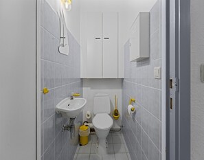 Et lille badeværelse med vask, toilet og skab.